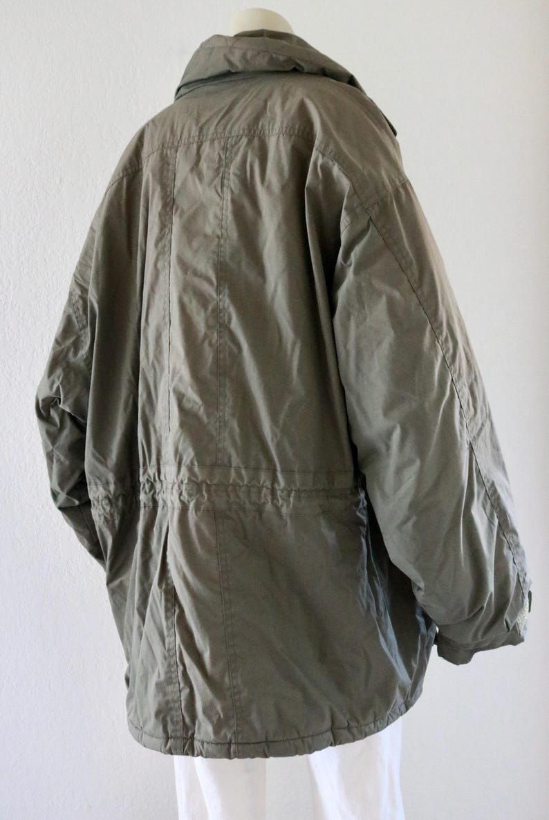Pu&ograve; includere: Giacca parka verde oliva con vita regolabile con coulisse e collo alto. La giacca ha una vestibilit&agrave; ampia e maniche lunghe. Vista posteriore che mostra i dettagli delle cuciture. Capo di abbigliamento classico.
