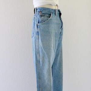 May include: Light blue denim jeans with a white knotted top and a straw hat. The jeans have a classic fit with front pockets. The outfit is displayed on a mannequin against a white background. The hat is brown.