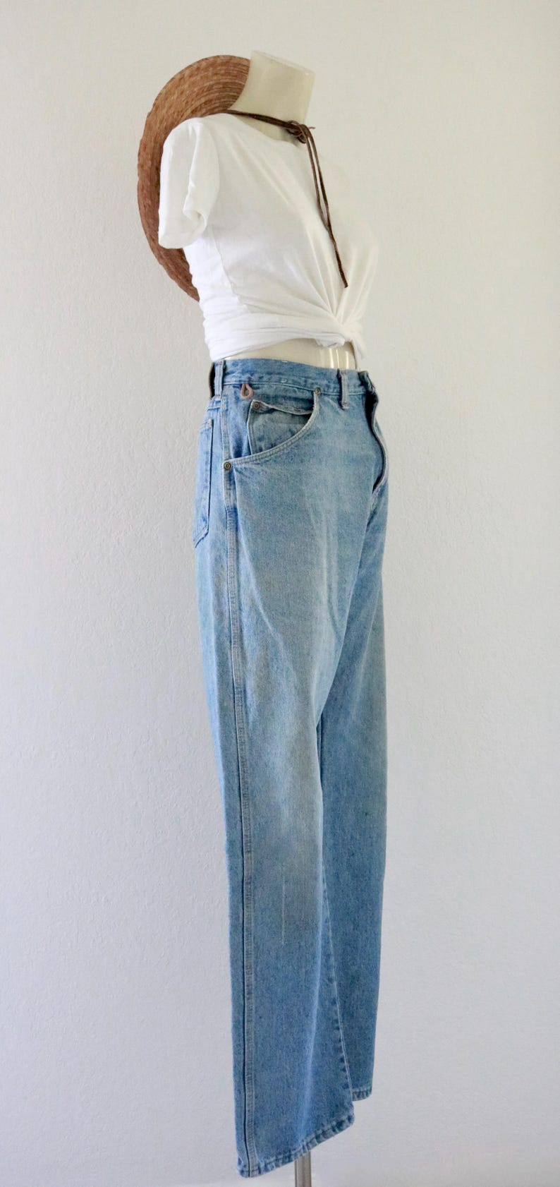 May include: Light blue denim jeans with a white knotted top and a straw hat. The jeans have a classic fit with front pockets. The outfit is displayed on a mannequin against a white background. The hat is brown.