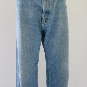 May include: Light blue denim jeans with a classic five-pocket design. The jeans have a button and zipper closure, belt loops, and a straight leg fit. The denim has a faded wash for a vintage look.