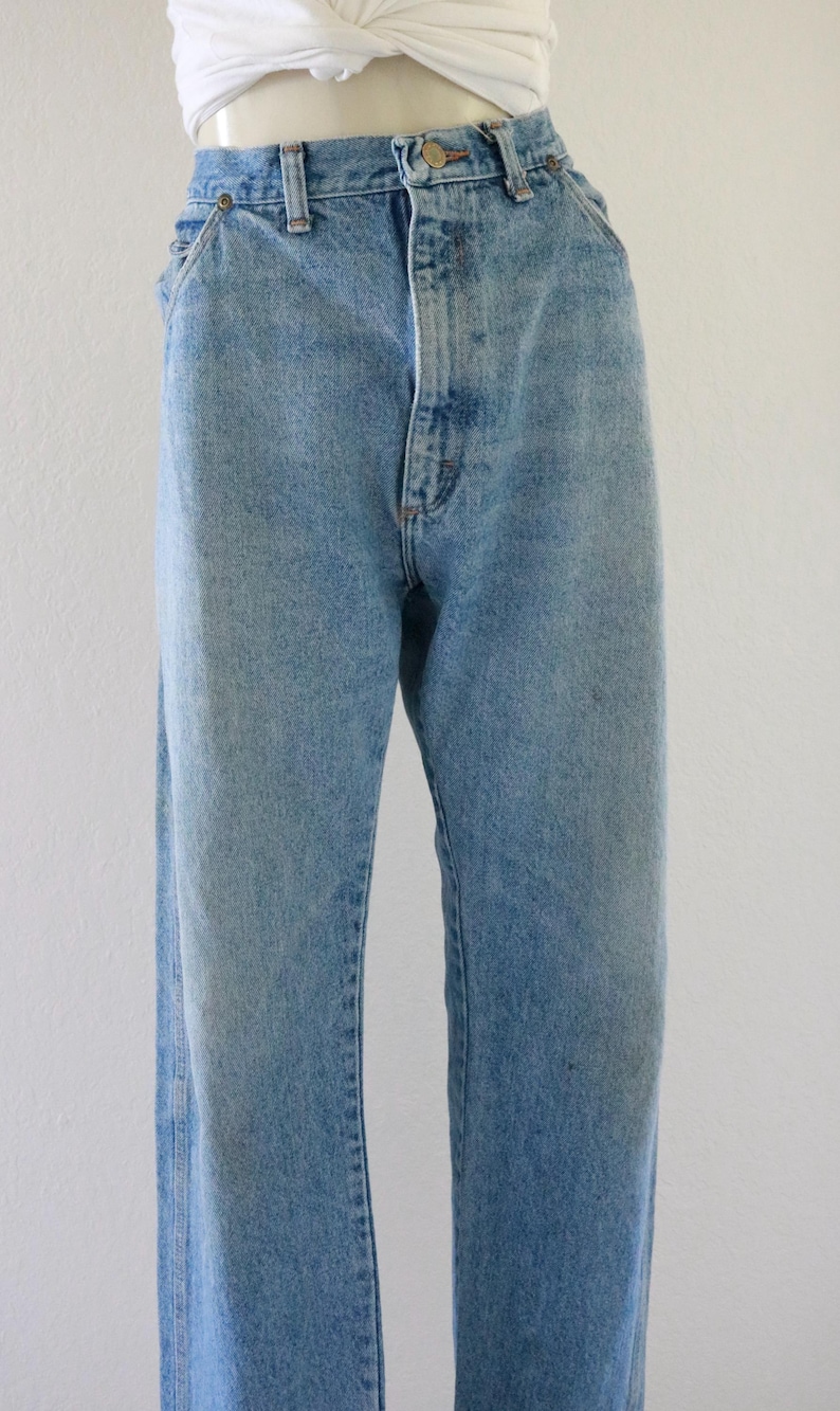 May include: Light blue denim jeans with a classic five-pocket design. The jeans have a button and zipper closure, belt loops, and a straight leg fit. The denim has a faded wash for a vintage look.