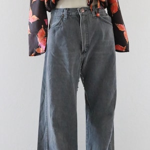 Puede incluir: Un maniqu&iacute; exhibe una blusa negra con un estampado floral rojo y naranja, combinada con vaqueros grises. Los vaqueros tienen cintura alta y pernera ancha. Un sombrero de paja est&aacute; encima.