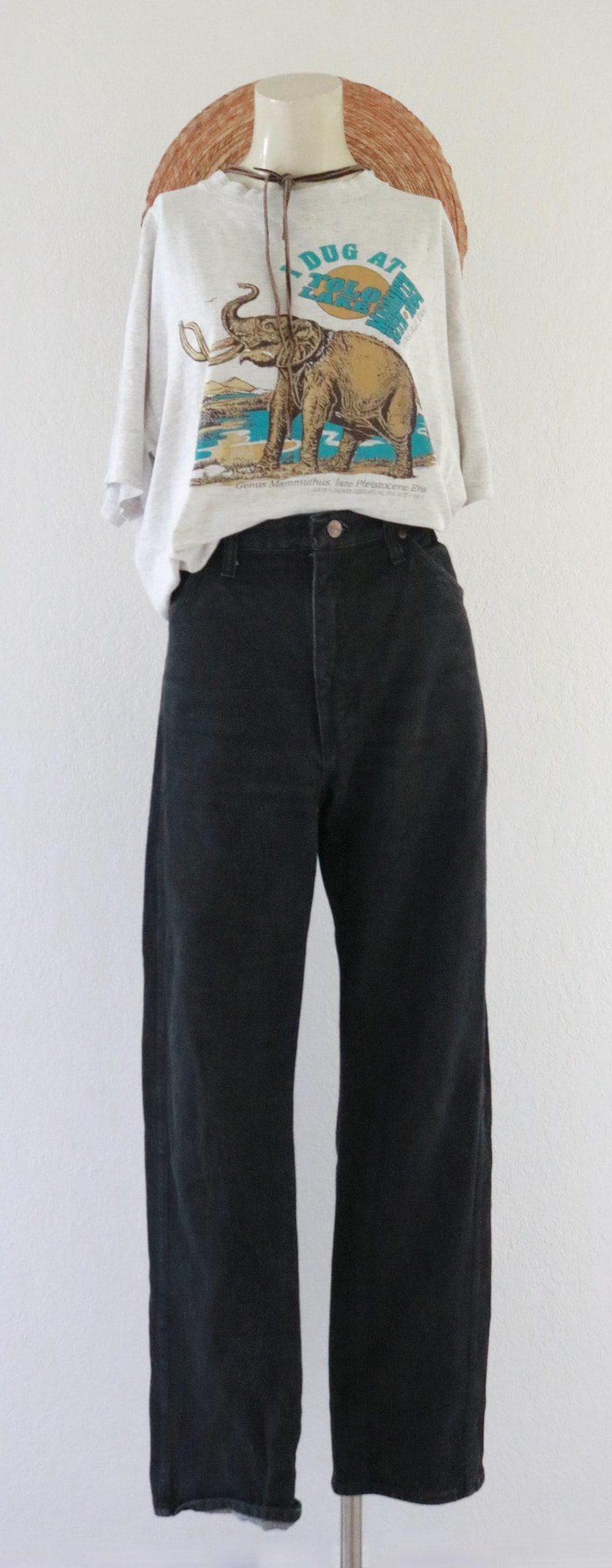 Puede incluir: Un maniqu&iacute; exhibe un atuendo casual. Presenta una camiseta gris claro con un gr&aacute;fico de un elefante y el texto "DUG AT ZPLO". El atuendo se completa con unos vaqueros negros. Un sombrero de paja est&aacute; encima.