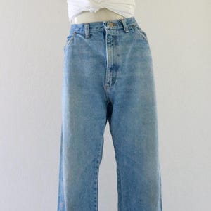 May include: A mannequin displays a casual outfit. It features light-wash denim jeans with a high waist and a white, knotted t-shirt. A straw hat with a brown cord is also included.