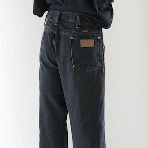May include: A person wearing a black t-shirt and dark wash denim jeans. The jeans have a brown leather patch on the back pocket. A straw hat with a brown band is worn.