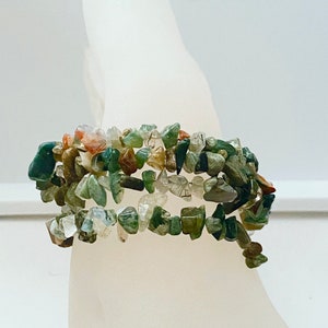 May include: A multi-strand bracelet made of green, brown, and clear chip stones. The bracelet is wrapped around a white mannequin hand.