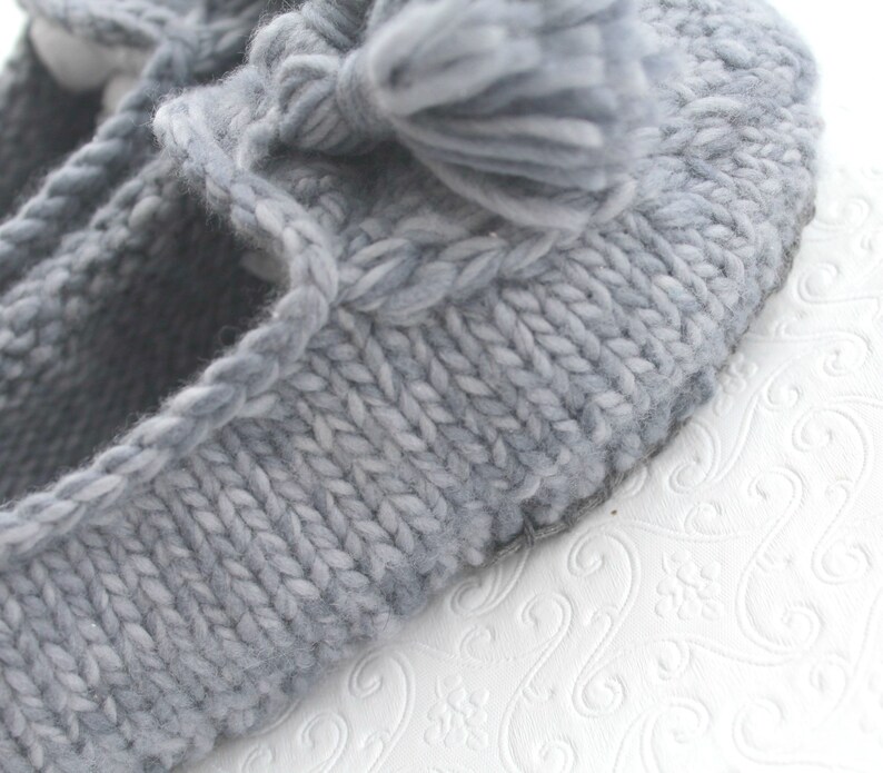 Puede incluir: Pantufla de punto gris con un pomp&oacute;n esponjoso en la parte superior. La pantufla tiene un dise&ntilde;o sencillo y est&aacute; hecha de hilo suave.