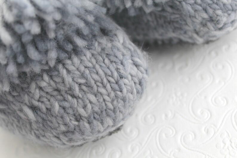 Puede incluir: Primer plano de un par de pantuflas de punto grises con textura peluda.