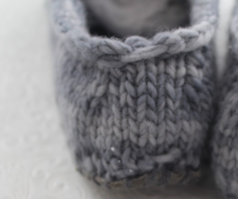 Puede incluir: Primer plano de un par de zapatillas de punto grises con un patr&oacute;n de motas blancas. Las zapatillas est&aacute;n hechas de un material suave y acogedor y tienen un dise&ntilde;o simple y cl&aacute;sico.