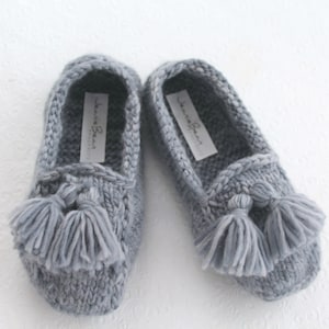 Puede incluir: Un par de zapatillas de punto grises con borlas. Las zapatillas tienen un dise&ntilde;o sencillo y est&aacute;n hechas de un material suave y c&oacute;modo. El nombre de la marca "Jeanne Bean" est&aacute; impreso en el interior de cada zapatilla.