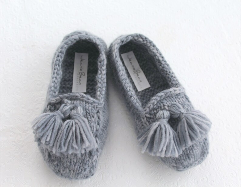 Puede incluir: Un par de zapatillas de punto grises con borlas. Las zapatillas tienen un dise&ntilde;o sencillo y est&aacute;n hechas de un material suave y c&oacute;modo. El nombre de la marca "Jeanne Bean" est&aacute; impreso en el interior de cada zapatilla.