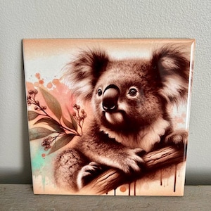 May include: A watercolor painting of a koala bear sitting on a branch with green leaves and pink and blue watercolor splatters in the background.