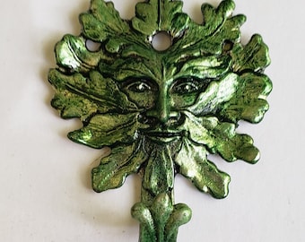 Puede incluir: Gancho de pared de metal verde con forma de Hombre Verde con una corona de hojas y una cara sonriente.
