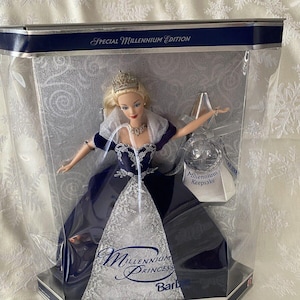 May include: A Special Millennium Edition Barbie doll in a display case. The doll wears a navy blue gown with silver accents and a tiara. The packaging includes the text "Millennium Princess" and "Millennium Keepsake".