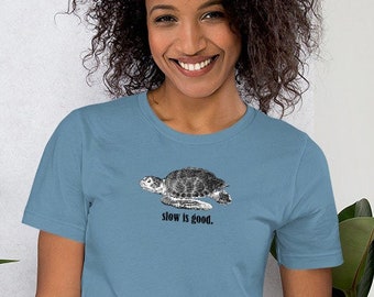 May include: A light blue t-shirt with a black and white illustration of a sea turtle and the text "slow is good."