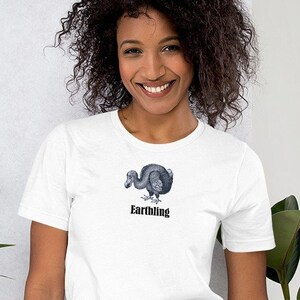 Op de afbeelding: Een wit T-shirt met een zwart-witte illustratie van een dodo en de tekst "Earthling" op de voorkant.