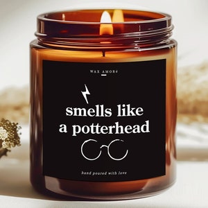 May include: A brown glass candle with a black label that reads "smells like a potterhead" with a lightning bolt and glasses graphic. The candle is lit and the wax is melting.