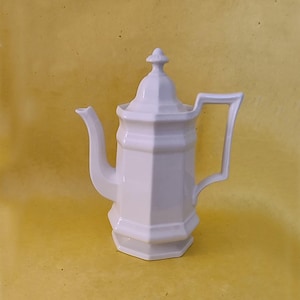 May include: White ceramic coffee pot with a lid and a handle. The pot has a geometric design and a smooth, glossy finish.