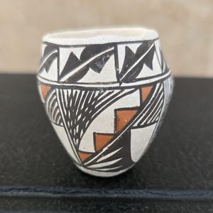 May include: Small, hand-painted ceramic pot with a white base and intricate black and orange geometric designs. The pot features a rounded body and a wide opening, showcasing traditional Native American artistry.