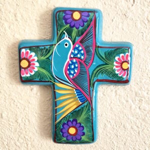 May include: Hand-painted, turquoise cross featuring a vibrant bird design. The bird has blue, pink, and yellow details, surrounded by green foliage and colorful flowers. A decorative piece with a folk art aesthetic.