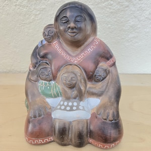 May include: A terracotta sculpture of a mother and her three children. The mother is seated with her arms around her children. The sculpture is painted in brown, red, green, and white.