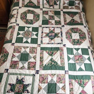 May include: A patchwork quilt featuring a repeating grid of square blocks in shades of forest green, white, and floral patterns. The design incorporates star motifs, geometric shapes, and striped fabric accents, all joined by white sashing.