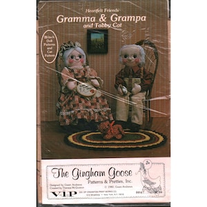 May include: A sewing pattern package titled Heartfelt Friends Gramma & Grampa and Tabby Cat, featuring two 22-inch fabric dolls in chairs with a small cat, an oval rug, and text including The Gingham Goose Patterns & Pretties, Inc. 1980.