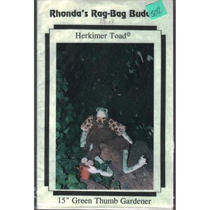 May include: A craft pattern titled Rhonda's Rag-Bag Buddies Herkimer Toad 15" Green Thumb Gardener. The cover features a photograph of a stuffed green toad doll wearing brown checkered overalls and a patterned shirt, sitting on a rock.