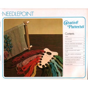 May include: A needlepoint instruction book titled Creative Patterns with a wooden frame holding a canvas featuring a floral design and a wooden thread organizer with various colored yarn strands in red, orange, yellow, green, and blue hues.