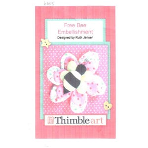 Puede incluir: Un adorno floral rosa y blanco con un diseño de abeja. La imagen incluye el texto "Free Bee Embellishment" y "Designed by Ruth Jensen". El adorno está decorado con botones en forma de estrella y corazón. También es visible el texto "Thimble art".