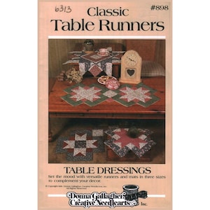 May include: A product catalog cover featuring the text "Classic Table Runners" and "Table Dressings." The image showcases various quilted table runners and mats in star and geometric patterns, with a wooden clock and decorative items.