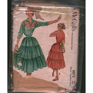 May include: A McCall's printed sewing pattern envelope for a two-piece dress, number 8873. The illustration shows two variations: a green long-sleeved dress with orange accents and a red short-sleeved dress, both featuring tiered, full skirts.