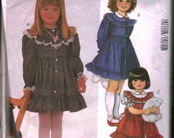 May include: Vintage McCall's sewing pattern for children's dresses. The pattern features illustrations of three different dress designs, including a gray dress with white lace trim, a blue dress, and a red dress. The pattern number is 2069.