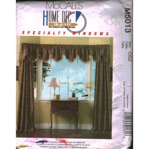 Puede incluir: Un sobre de patrón de costura McCall's Home Dec M5013 para ventanas especiales. La parte frontal muestra una cenefa y paneles laterales de color marrón con patrones sobre una ventana, con una mesa y lámpara. Texto: McCall's Home Dec In-A-Sec.