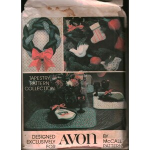 Op de afbeelding: Een vintage tapestry patrooncollectie exclusief ontworpen voor Avon. De afbeelding toont een kerstkrans met een rode strik, een versierde kerstboom en placemats. Het patroon is van McCall Patterns.