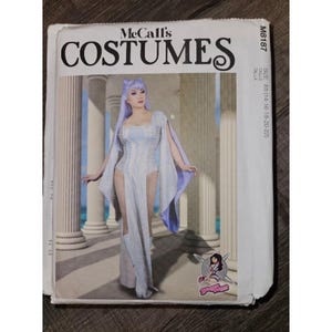 May include: A McCall's Costumes sewing pattern envelope M8187, size E5 (14-16-18-20-22). The front features a photograph of a person wearing a light purple, floor-length gown with long, flowing sleeves, a high-cut skirt, and matching boots.