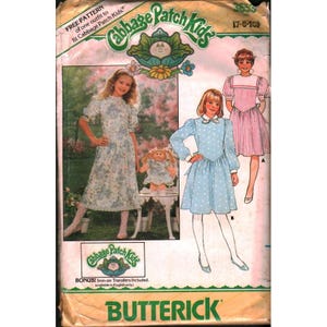 May include: Vintage Butterick sewing pattern for Cabbage Patch Kids outfits. The pattern shows illustrations of girls in dresses, including a floral print and a polka dot design. The package includes the text "FREE PATTERN" and "BONUS! Iron-on Transfers Included."