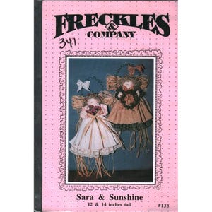 May include: A pink package featuring two handmade dolls, Sara and Sunshine, with straw hair and fabric dresses. The dolls are 12 and 14 inches tall. The package has the text "FRECKLES COMPANY" and "Sara & Sunshine".
