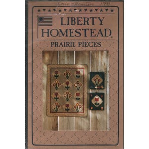 May include: A craft pattern booklet titled Liberty Homestead Prairie Pieces with a 1991 date. The cover features a rectangular quilt with a repeating floral diamond pattern and two smaller framed square wall hangings with floral motifs.