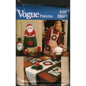 May include: Vogue Patterns 8753 Craft sewing pattern envelope featuring illustrations of Christmas-themed projects including a Santa wall hanging, gift bags with red hearts, a wreath-patterned apron, and a table runner with placemats.