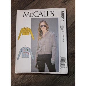 May include: McCall's M8011 sewing pattern envelope for a button-front jacket in size Z (LRG-XLG). The cover features illustrations of a yellow cropped jacket and a light blue denim-style jacket with patches, alongside a photo of a grey jacket.
