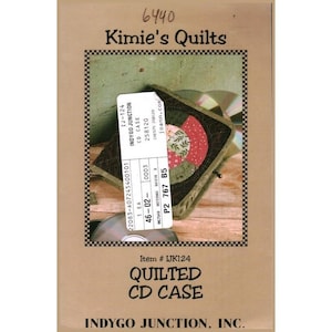 May include: A brown cardboard package featuring a quilted CD case. The case is dark green with a patchwork design in red, green, and cream. The package includes the text "Kimie's Quilts" and "Quilted CD Case."
