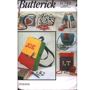 May include: A sewing pattern by Butterick, featuring various bag designs. The bags include a backpack with "JOE" on it, a heart-shaped bag, a dalmatian-print bag, and a blue bag with a red bow. The pattern also includes a red and blue bag with "LT".