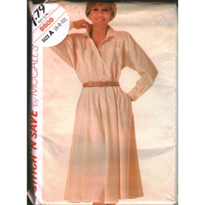 May include: A McCall's sewing pattern envelope for a long-sleeved, button-down shirt dress in a light cream color. The pattern, labeled 9509, features a collared neckline, two chest pockets, and a brown belt cinching the waist of the garment.