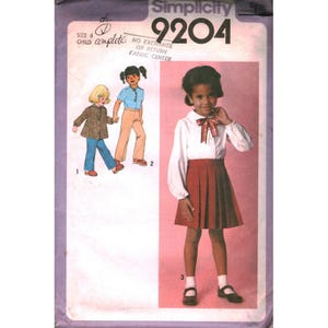 Puede incluir: Un sobre de patrón de costura Simplicity 9204 para un conjunto infantil de talla 6. La portada presenta ilustraciones de tres combinaciones de ropa diferentes, que incluyen una blusa blanca de manga larga con un lazo a cuadros y una falda plisada.