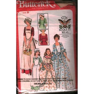 Pode incluir: Um pacote de padrões de costura Butterick vintage com ilustrações de vestidos históricos para mulheres e meninas. O pacote é tamanho 8, com o texto "1776 MAKE IT REAL" e o aviso "THIS BAG IS NOT A TOY".