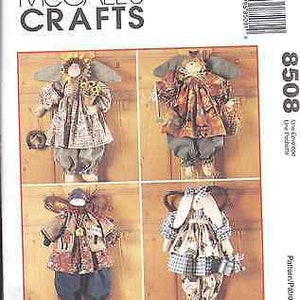 Könnte beinhalten: Nähmuster von McCall's Crafts Nummer 8508 für vier verschiedene Stoffpuppen. Die Puppen sind in verschiedenen Stoffen gekleidet und haben unterschiedliche Frisuren. Das Muster enthält Anweisungen zum Herstellen der Puppen und ihrer Kleidung.