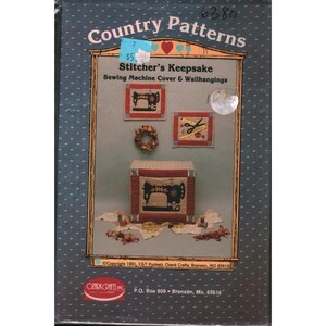 May include: A box for "Country Patterns" featuring a sewing machine cover and wall hangings. The box has a blue background with white dots. The front of the box shows a sewing machine cover, two wall hangings, and a small wreath. The text "Stitcher's Keepsake" is visible.
