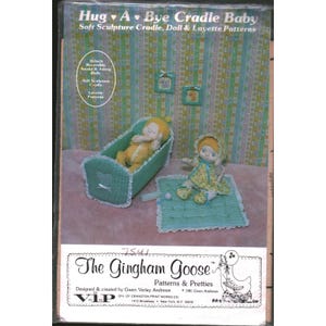 May include: A sewing pattern envelope titled Hug A Bye Cradle Baby by The Gingham Goose. The cover features a soft sculpture cradle, a 12-inch reversible awake and asleep doll, and layette patterns, all displayed in shades of green and yellow.