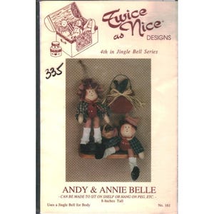 Może przedstawiać: Okładka wzoru rzemieślniczego z dwiema szmacianymi lalkami, Andym i Annie Belle, z "Jingle Bell Series". Lalki ubrane są w kraciaste i czerwone stroje, z małym koszykiem i wiszącą ozdobą. Tekst brzmi "Twice as Nice Designs", a lalki mają 20 cm wysokości.
